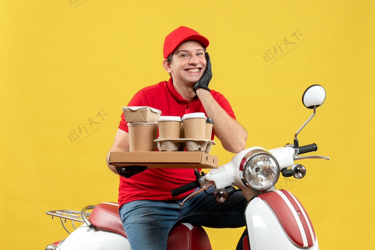 摩托车一个身穿红色上衣 戴着帽子 戴着手套 戴着医用口罩 面带微笑 满怀希望的快递员坐在滑板车上 手里拿着订单面罩滑板车微笑