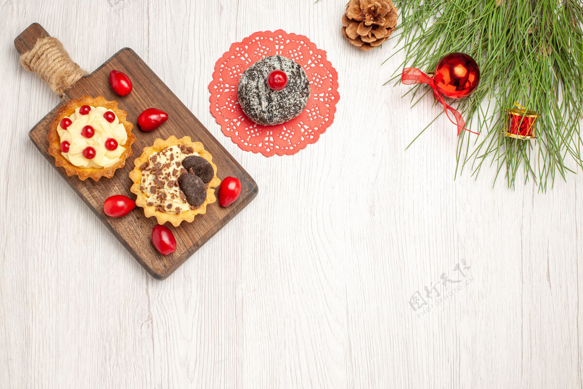圣诞俯瞰砧板上的可可 浆果馅饼和山茱萸可可蛋糕和松树叶子 白色木质地面上放着圣诞玩具食物木头地