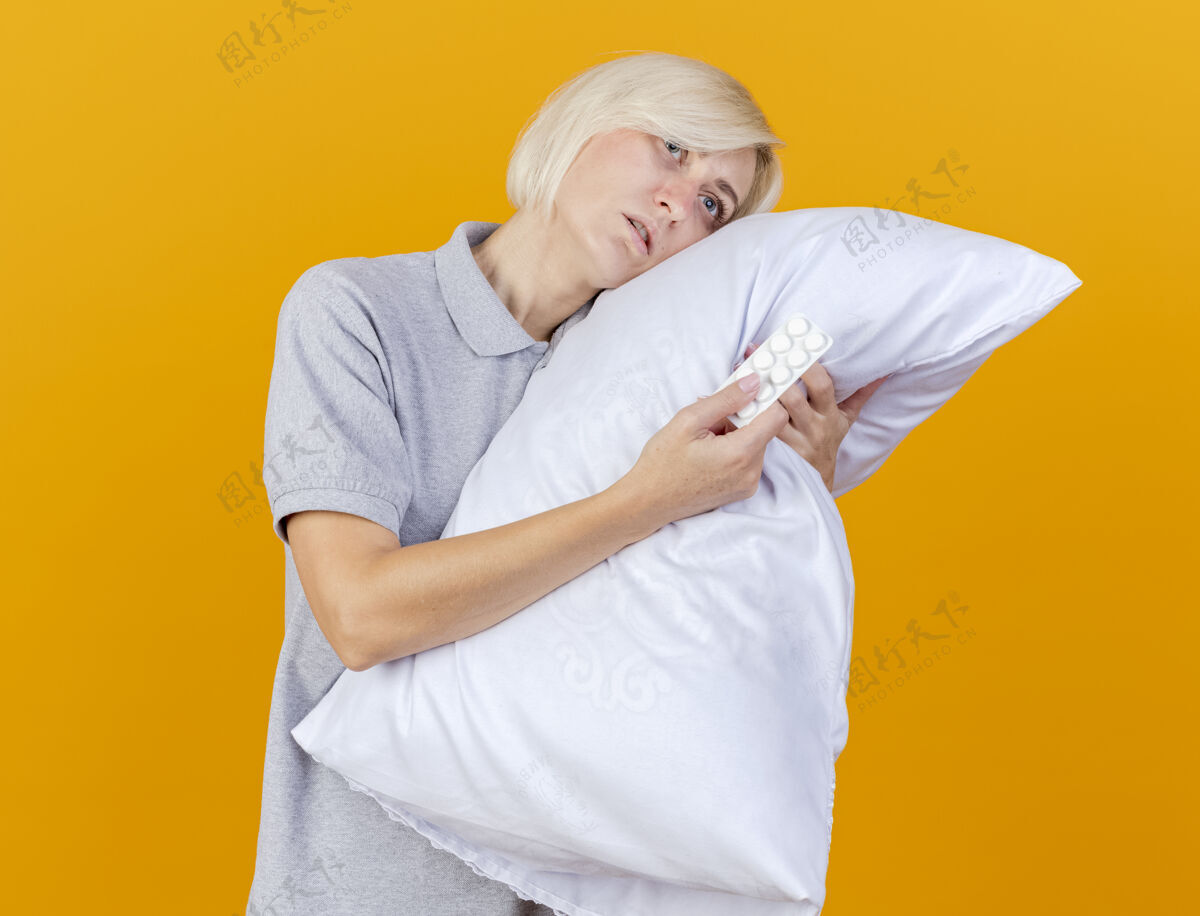 市民脸色苍白的年轻金发病女人把头靠在枕头上拿着一包隔离在橙色墙上的药丸斯拉夫表情金发