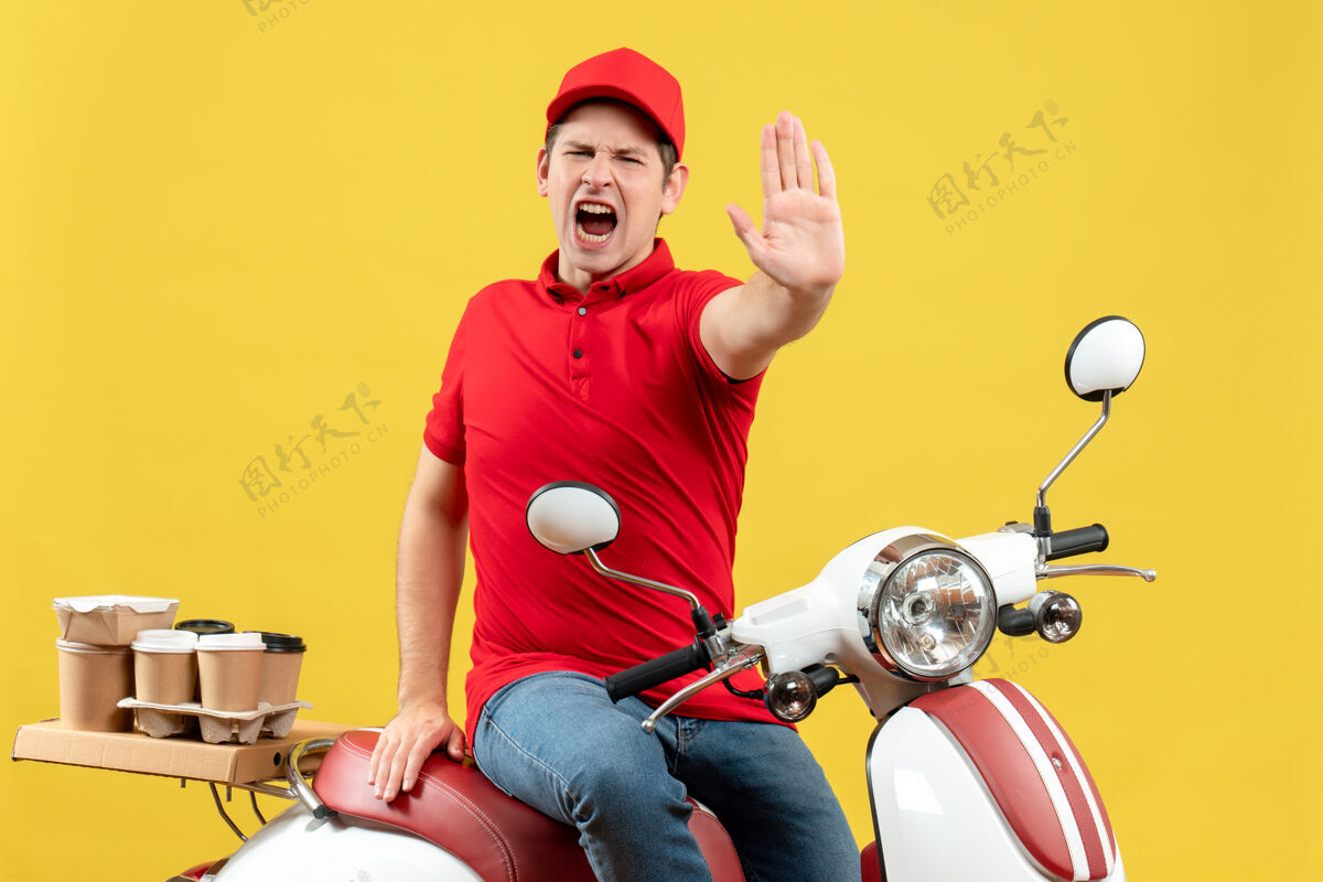 黄色顶视图愤怒的年轻人穿着红色上衣 戴着帽子 在黄色背景下发出停止手势的命令摩托车显示男人