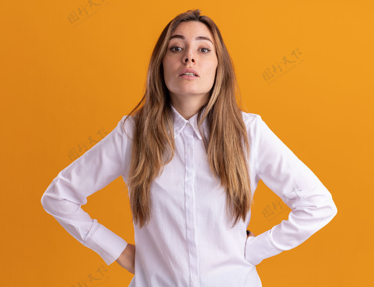 手自信的年轻漂亮的白人女孩把手放在腰上 看着橙色的相机腰漂亮自信