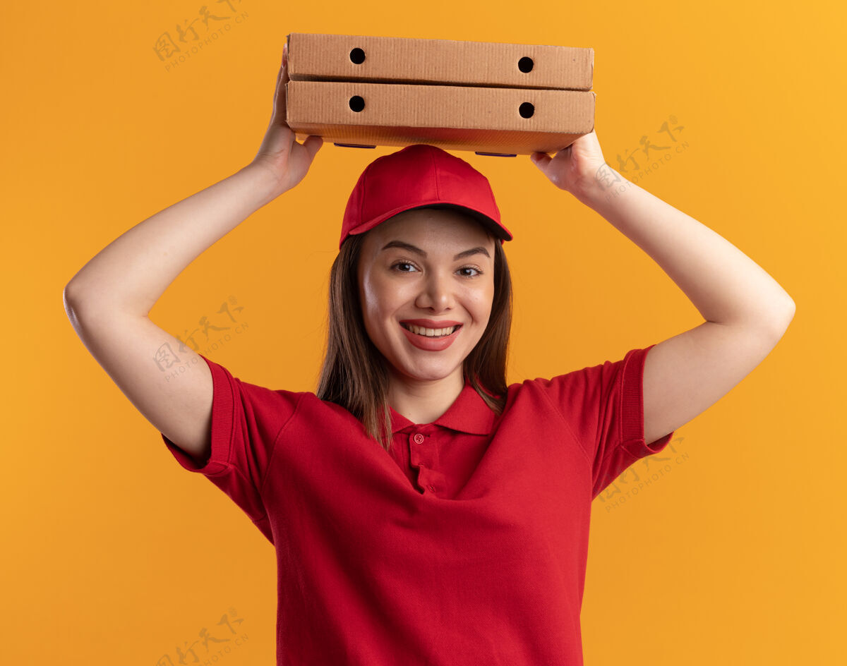 橘子身着制服的微笑漂亮的女送货员把披萨盒举过头顶放在橘子上头制服盒子