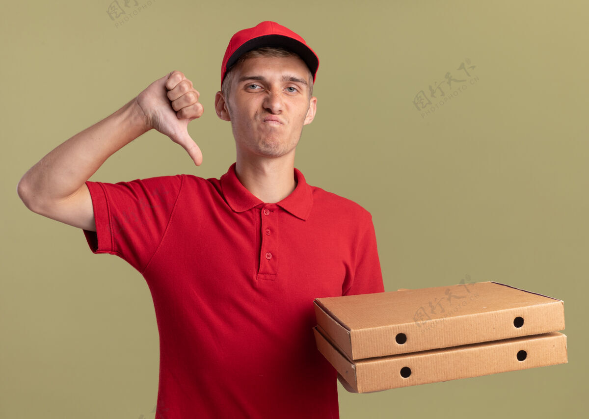 拇指年轻的金发送货员拇指朝下 拿着橄榄绿的披萨盒不愉快橄榄向下