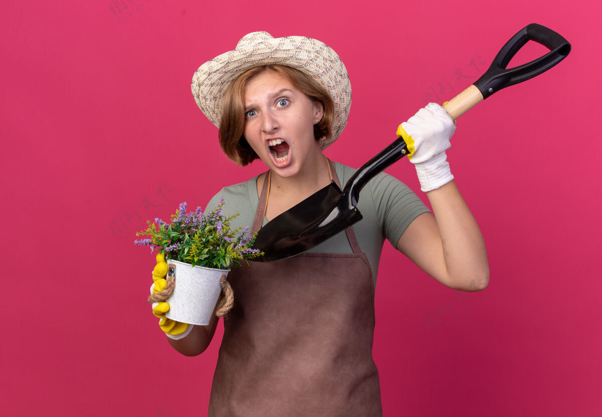花园恼怒的年轻斯拉夫女园丁戴着园艺帽和手套 手里拿着花盆里的花和粉红色的铲子恼怒女性手套