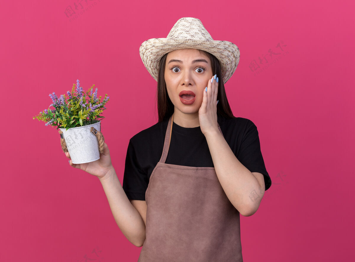 漂亮焦急漂亮的白人女园丁戴着园艺帽 手放在脸上 手里拿着粉红色的花盆女帽子手