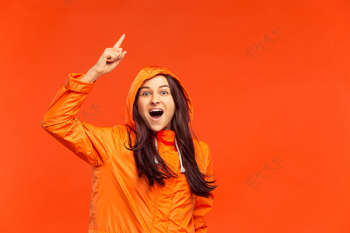 持有在摄影棚里 一个快乐微笑的小女孩穿着秋天的橙色夹克 指着孤立的红色人类积极的情感寒冷天气的概念女性时尚的概念聪明季节安全