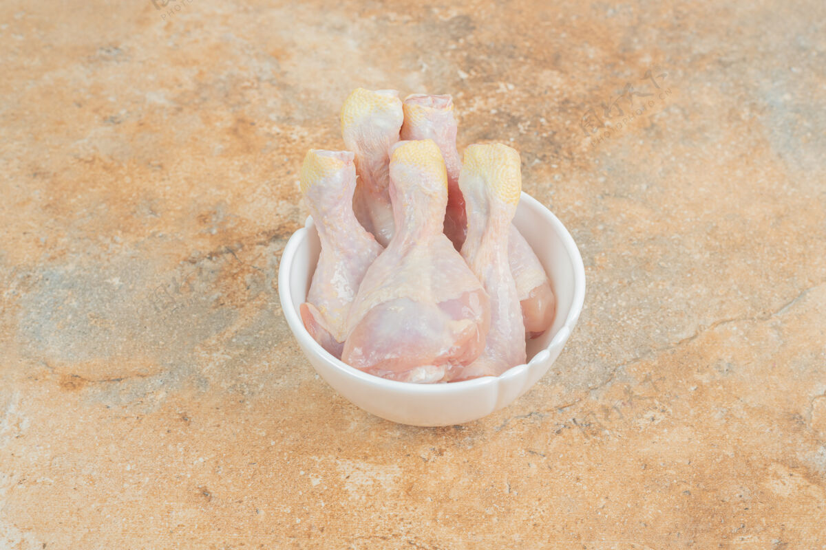 生的未经料理的鸡腿放在大理石表面的白色盘子里生的鸡肉腿
