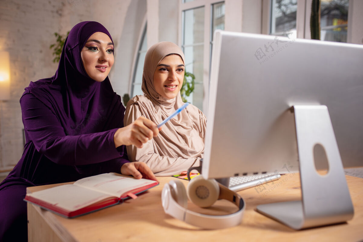 肖像快乐的两位穆斯林妇女在家上课 在电脑旁学习 在线教育女人房子女性