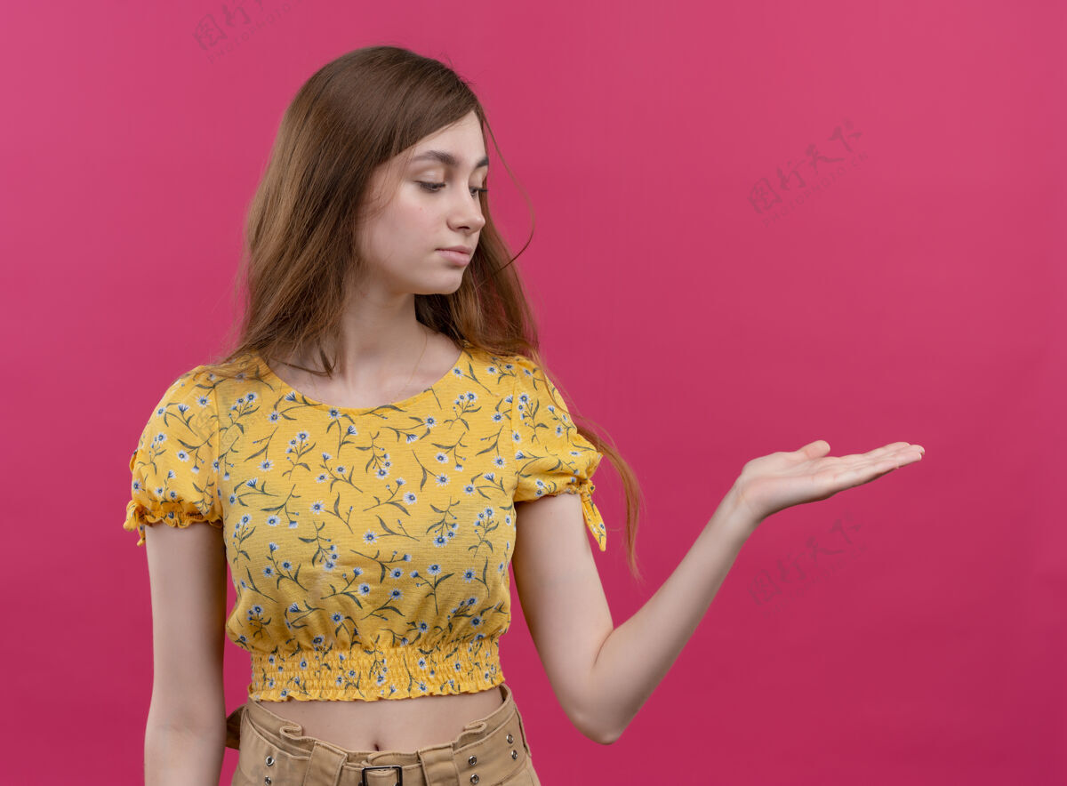 壁板严肃的年轻女孩显示空手 并在孤立的粉红色空间看右侧女孩右手