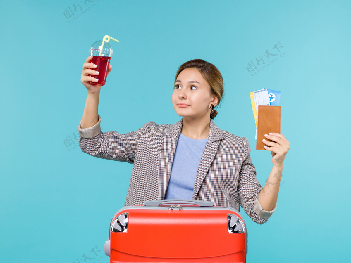 樱桃正面图：度假中的女性手持新鲜的樱桃汁和蓝色背景的机票旅行旅行飞机旅行成人女人果汁