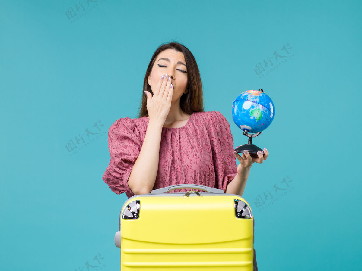 肖像前景度假中的女性手持小地球仪 在蓝色背景上打呵欠旅行海上女性旅行度假暑假哈欠地球旅行