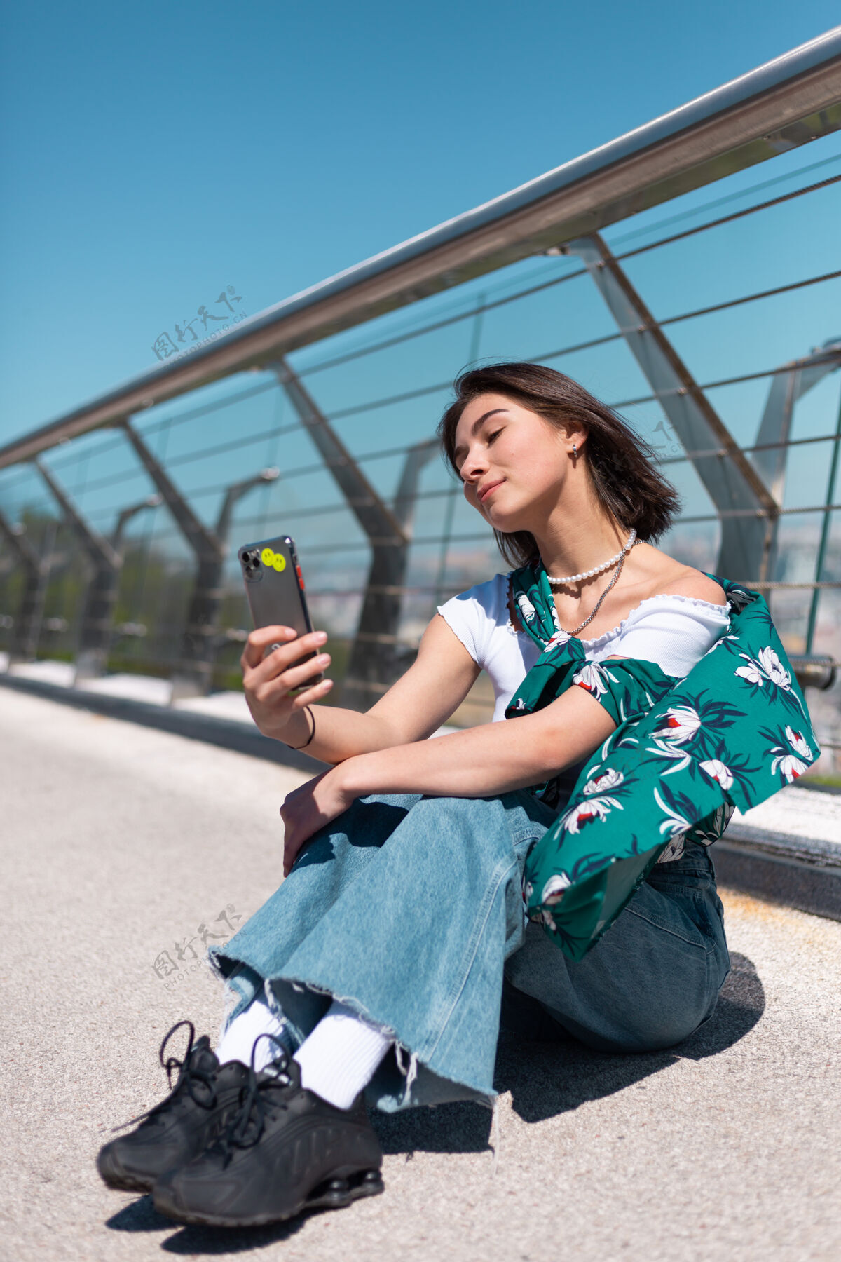 聊天阳光明媚的日子里穿着休闲绿衬衫的女人站在桥上看手机屏幕的户外肖像自拍打视频电话城市电话复制空间