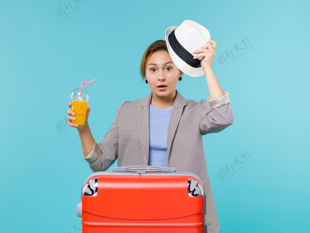 假期正面图：度假中的女性手持新鲜果汁 戴着帽子在蓝色背景下出海度假肖像前面旅行