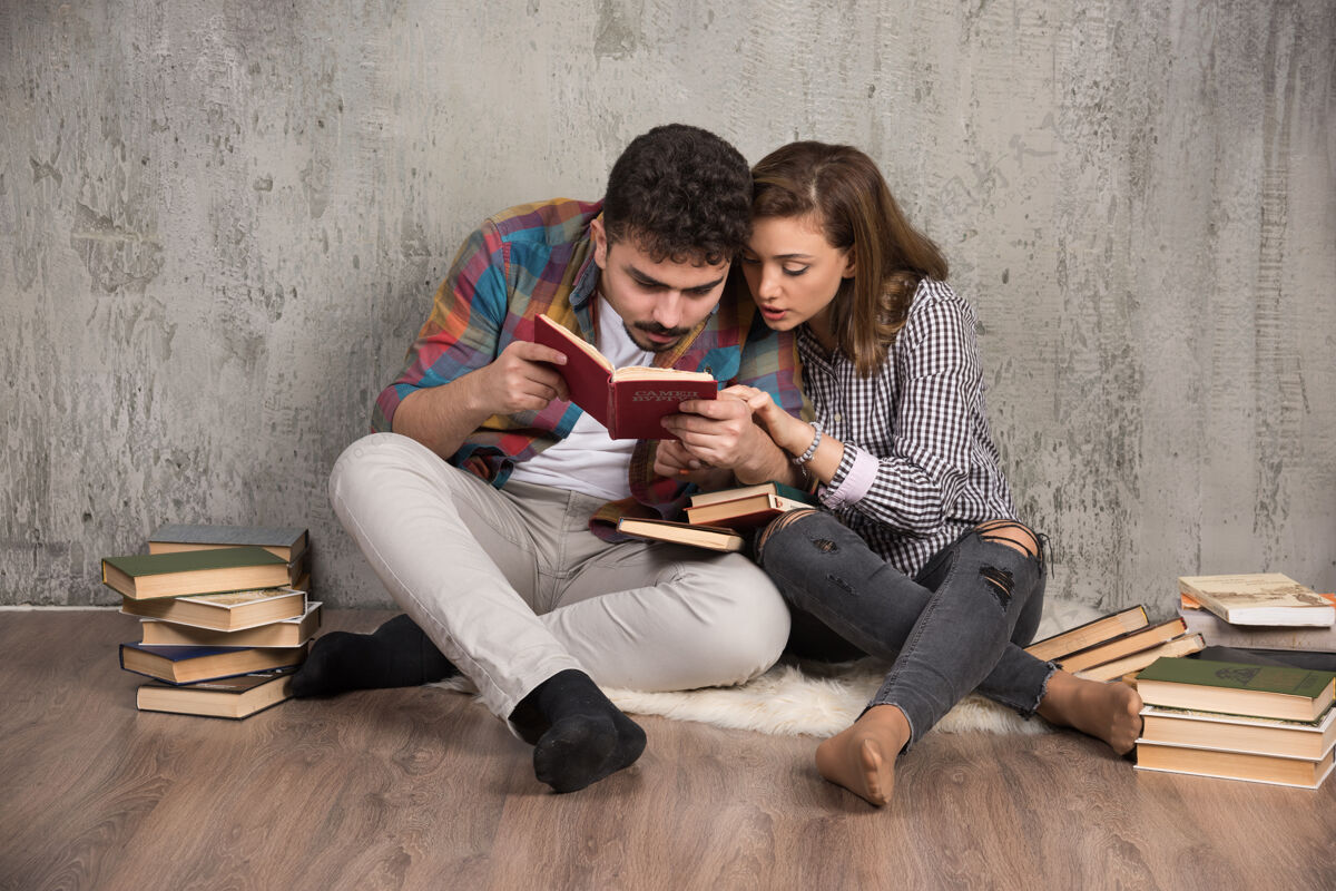 文学一对年轻夫妇坐在地板上看一本有趣的书家庭生活讨论坐着