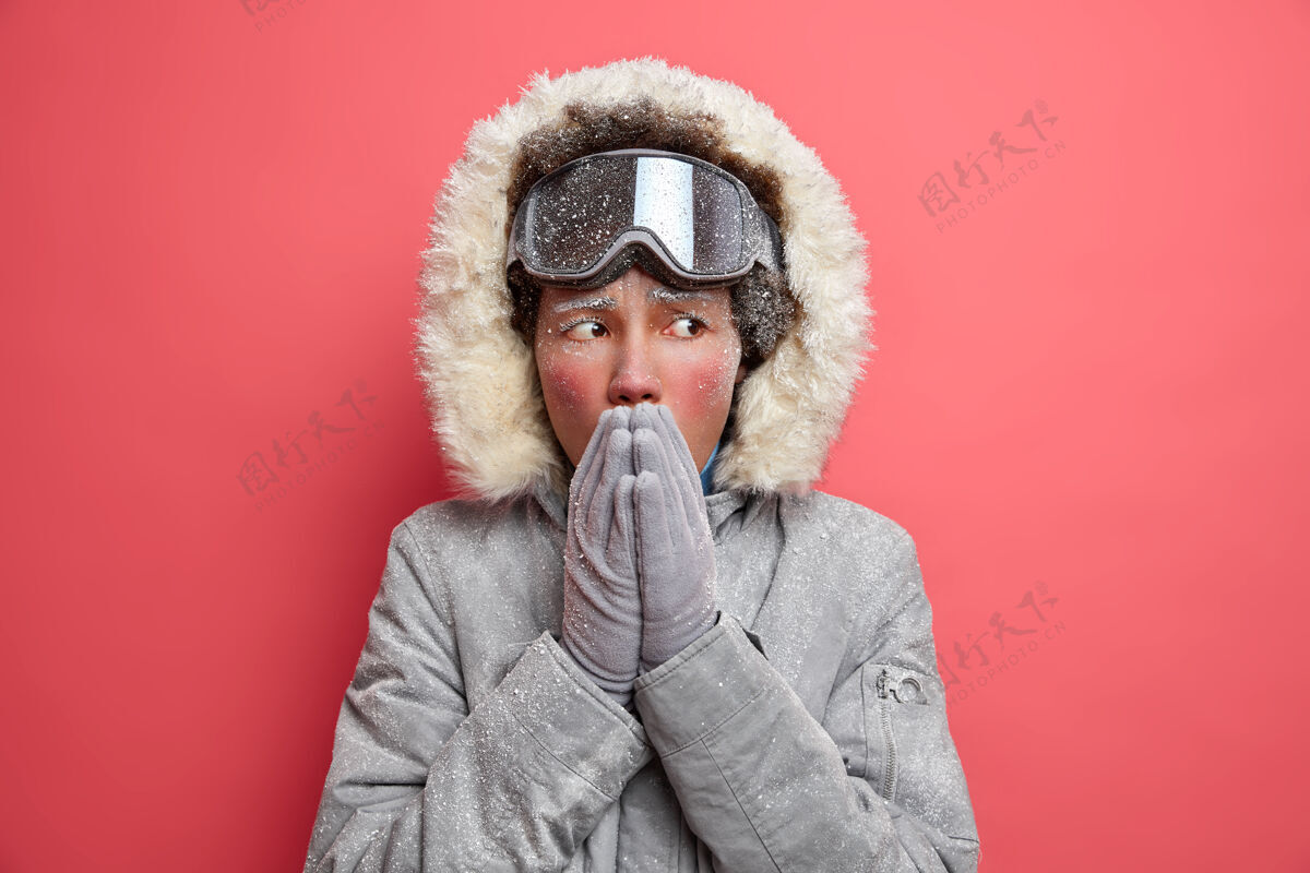 霜冻冬天的照片被冻的少数民族妇女通过吹热空气温暖被冻的手感觉寒冷在寒冷的天穿着暖和的外套有积极的休息戴滑雪护目镜肖像季节帽子