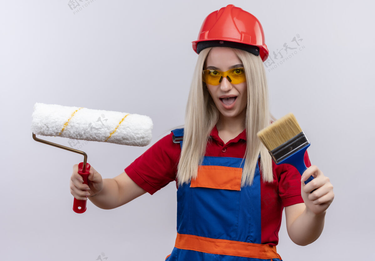 滚轴令人印象深刻的年轻金发工程师建设者穿制服的女孩戴着安全眼镜拿着油漆刷和辊在孤立的白色空间印象工程师安全