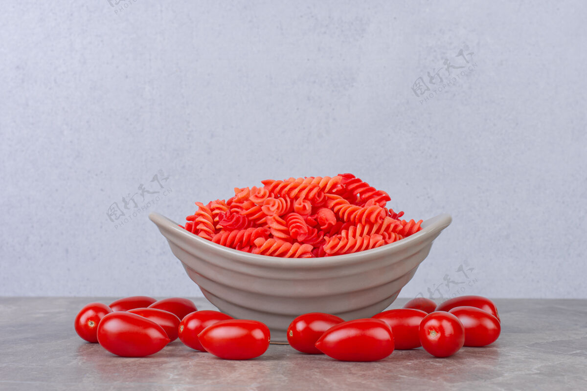 烹饪把生的红色意大利面放在番茄旁边的碗里 放在大理石表面滋补干燥营养