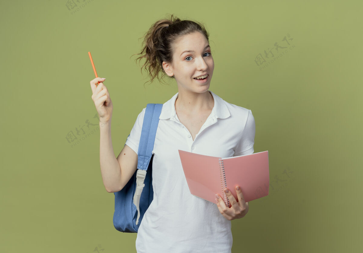 背景令人印象深刻的年轻漂亮的女学生穿着背袋举行记事本和提高孤立的橄榄绿背景笔包提高绿色