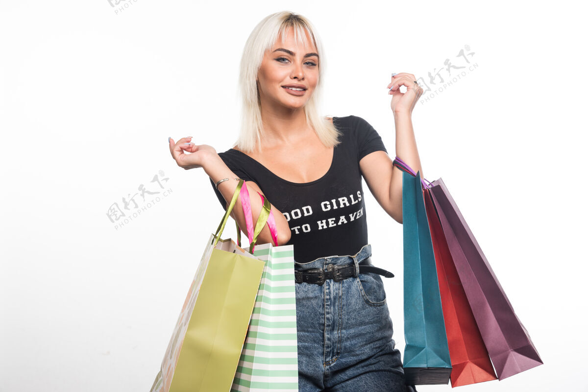 休闲年轻女子拿着购物袋站在白色的墙上 表情愉快购物者成人携带