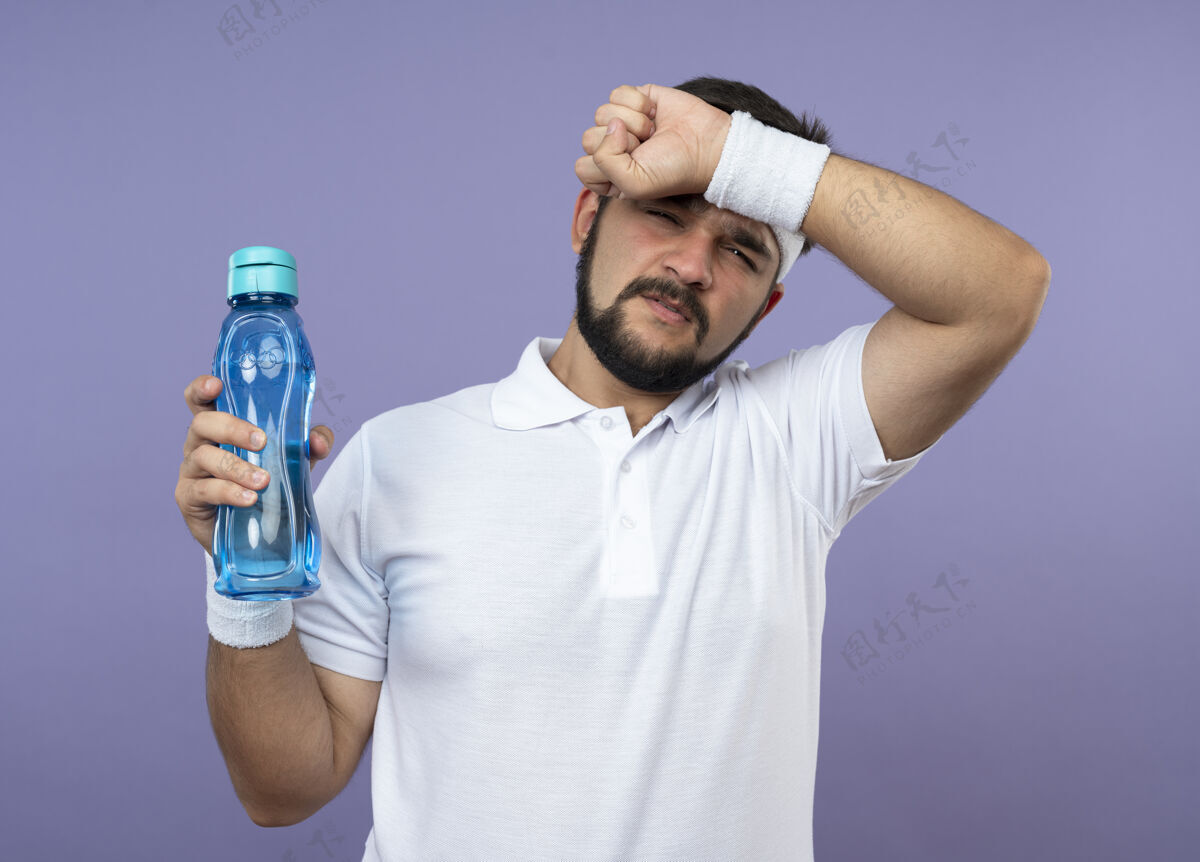 水戴着头带和腕带 拿着水瓶 手放在额头上的一个不讨人喜欢的年轻人不愉快男人戴