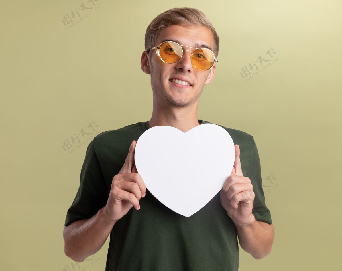 形状微笑着的年轻帅哥 穿着绿色衬衫 戴着眼镜 拿着心形盒子 孤立在橄榄绿的墙上感觉抱着微笑