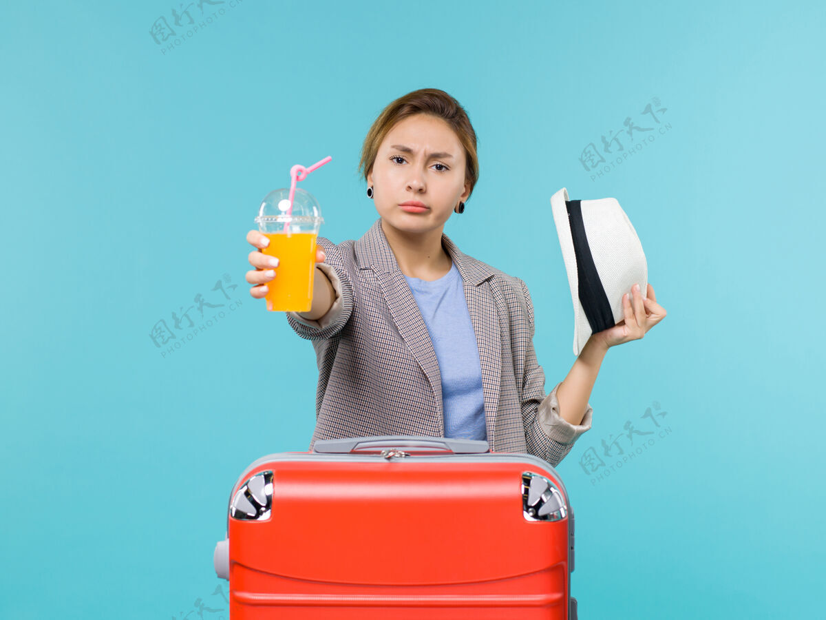 工人正面图：度假中的女性拿着新鲜果汁和她的帽子在蓝色背景上远航海上度假之旅帽子旅行人