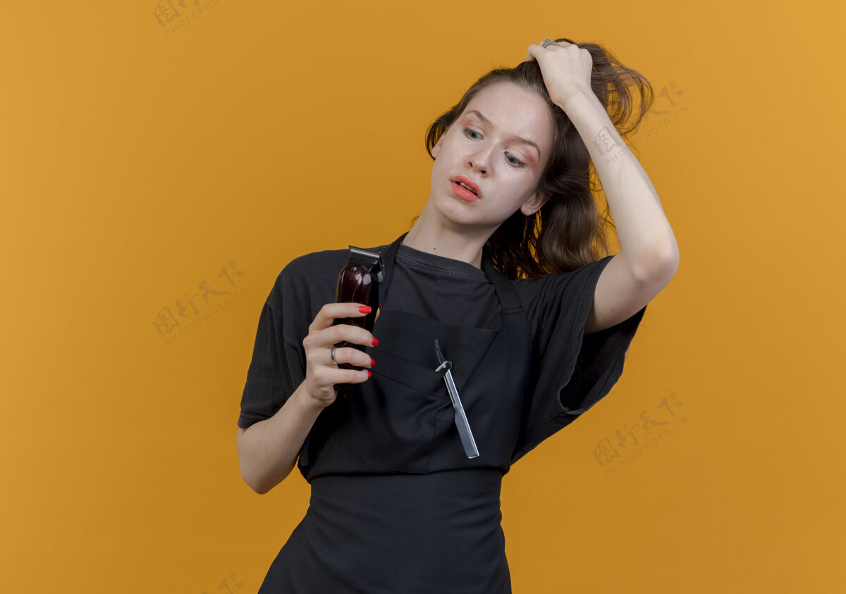 理发师令人印象深刻的年轻斯拉夫女理发师穿着制服拿着 看着剪子和拉头发孤立的橙色背景与复制空间剪女背景