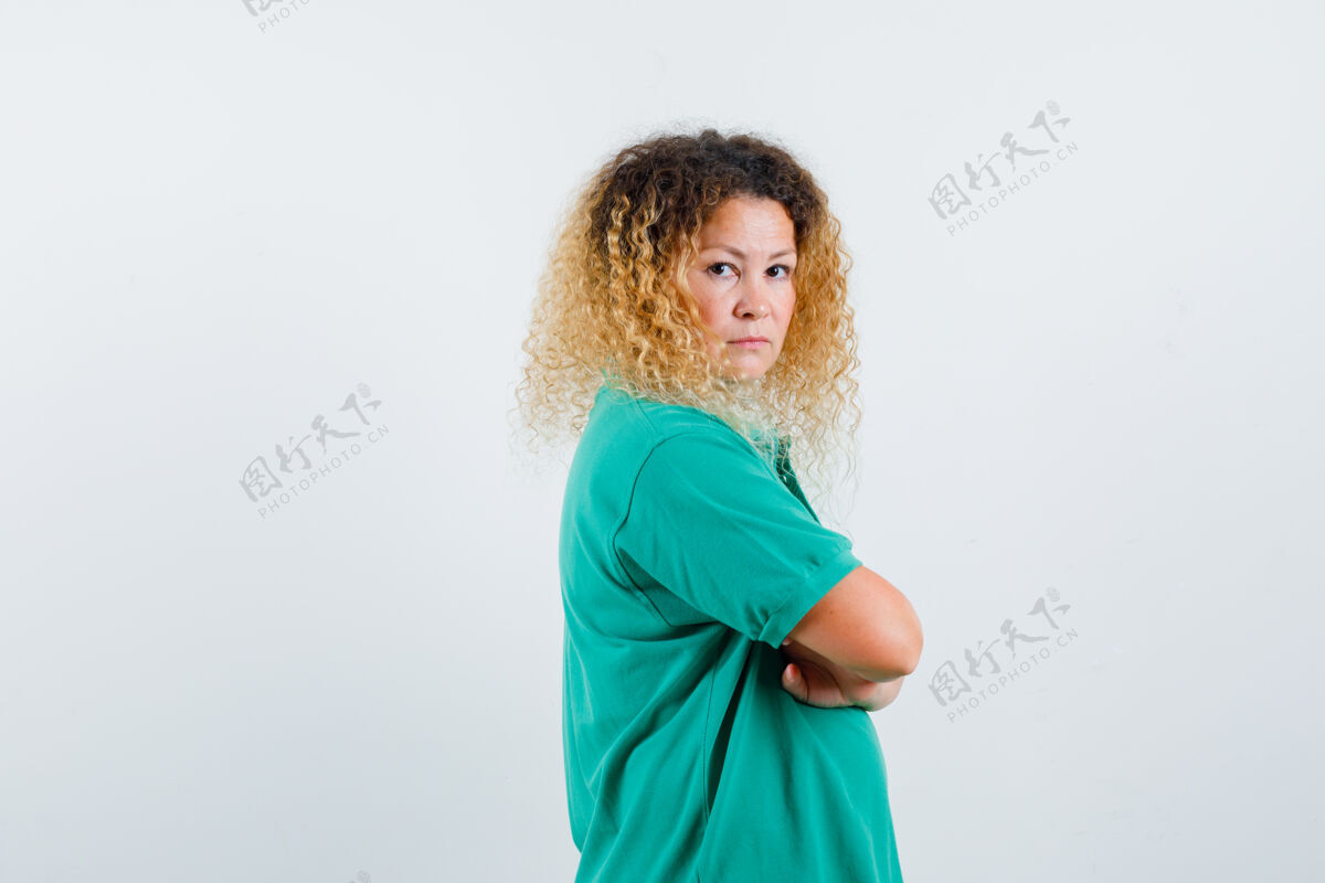 时尚美丽的金发女人的肖像保持双臂交叉在绿色马球t恤 看起来很严肃人站立漂亮