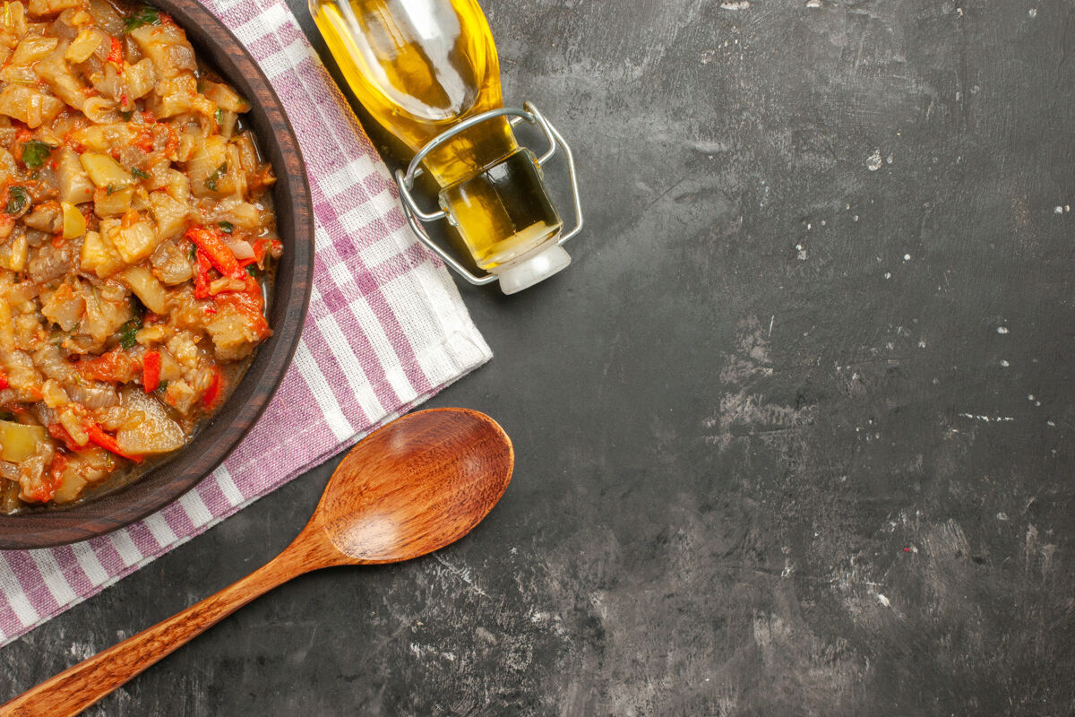 盘子在黑暗的表面上用碗油和木勺烤茄子沙拉的俯视图黑暗午餐健康