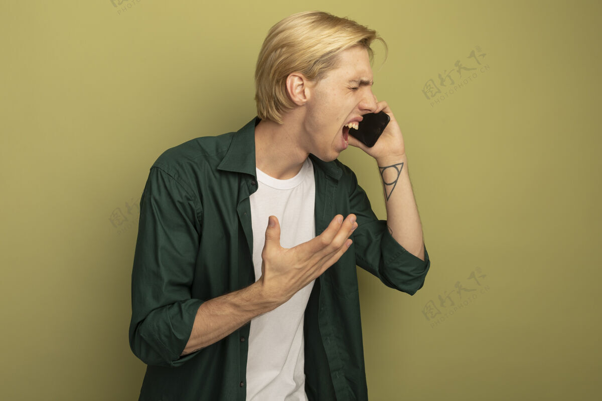 男人愤怒的闭着眼睛年轻的金发小伙子穿着绿色t恤在电话里讲话眼睛年轻穿