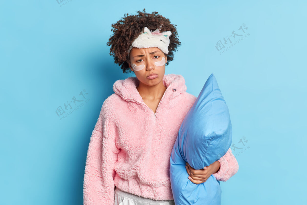 姿势不满卷发的美国黑人年轻女子想睡觉抱着枕头准备睡觉睡眠面具美女肖像
