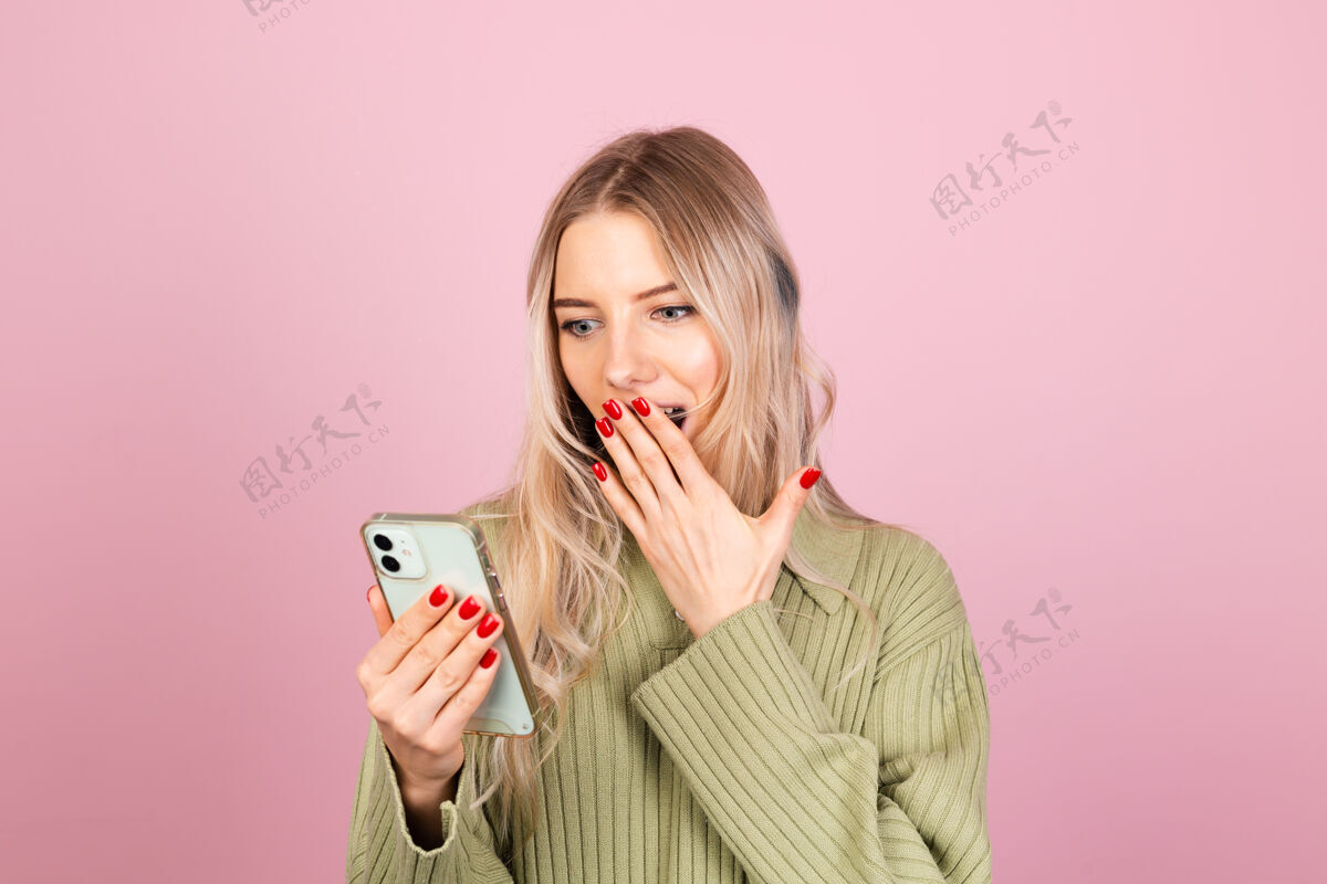 手机漂亮的欧洲女人在粉红色的墙上穿着休闲针织毛衣请电话美丽