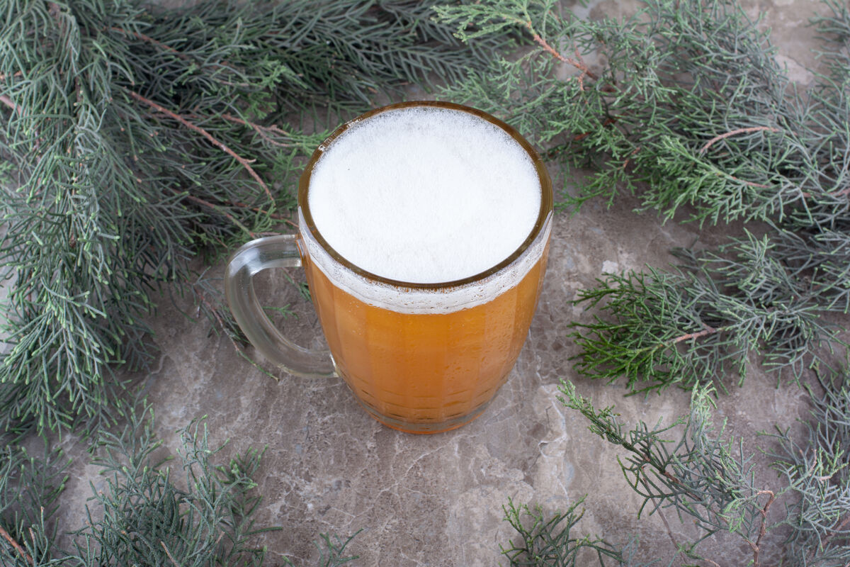 刷新一杯啤酒放在大理石表面和松枝上松枝泡沫顶视图