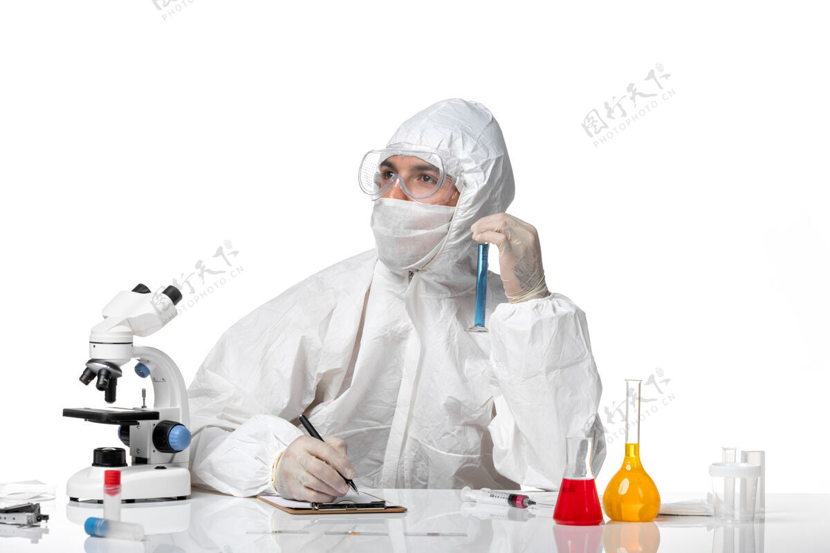 医疗正面图：男医生穿着防护服 戴着面罩 因为covid拿着蓝色溶液写在空白处的烧瓶面罩外套防护