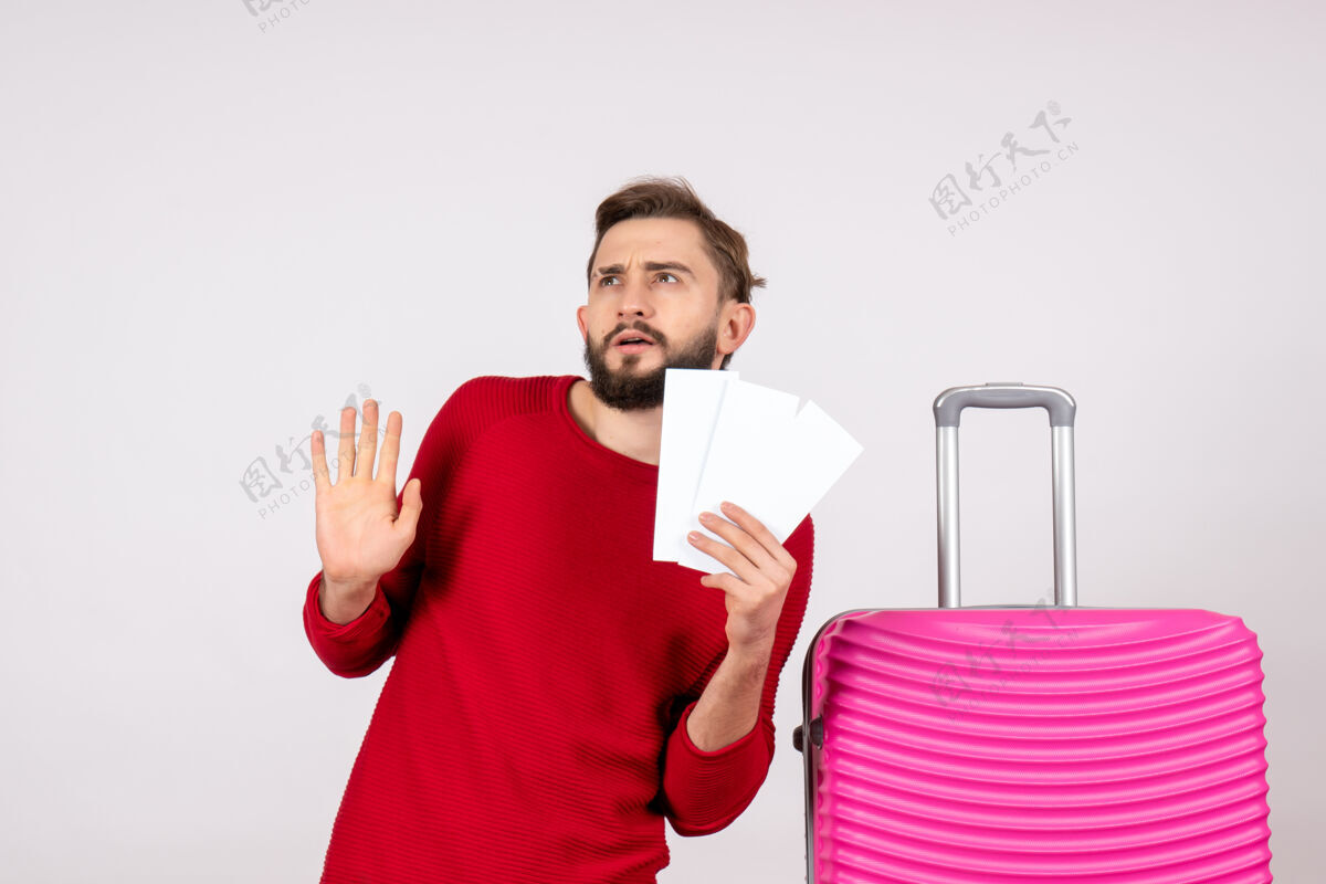成人正面图年轻男性手拿粉红包 手拿机票上白墙远航航班彩色旅游度假照片感慨游客机票男人