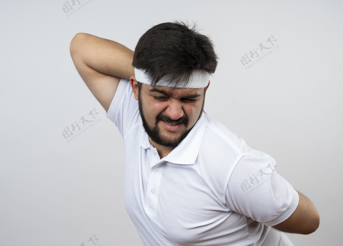 封闭疲惫的年轻运动男子闭着眼睛戴着头带和腕带把手放在腰上隔离在白墙上穿手运动