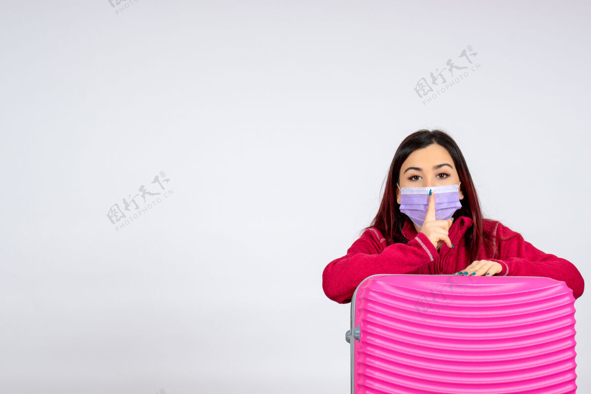 年轻女性正面图：年轻女性带着粉色袋子 在白色墙壁上戴着无菌口罩 旅行时携带彩色柯维德病毒——女性病毒大流行颜色成人女人
