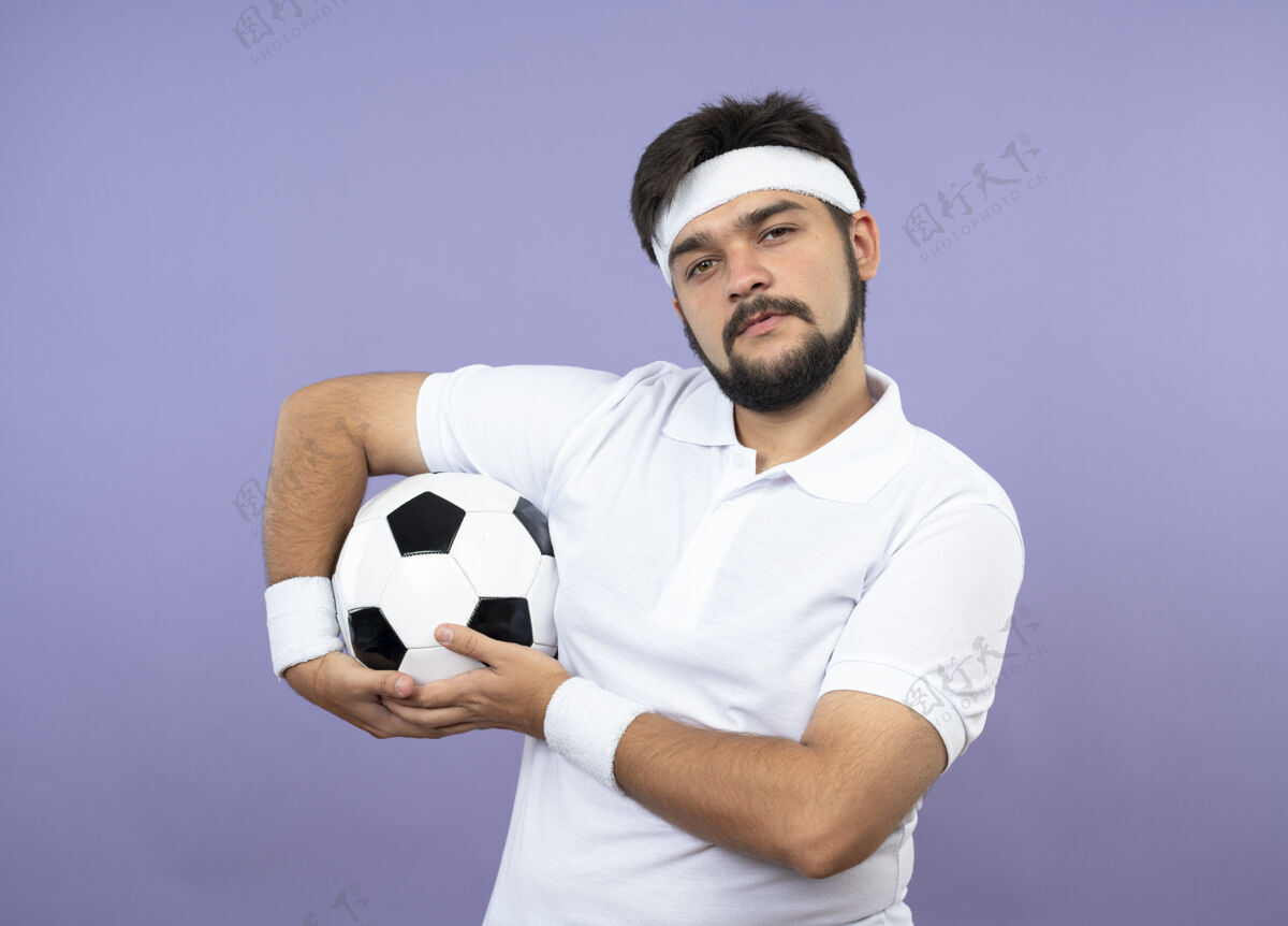 手持高兴的年轻人戴着头带和手环举行球隔离在绿色的墙壁上运动运动型男请戴