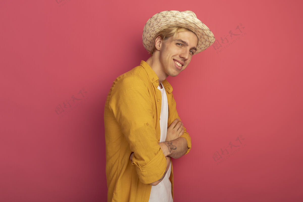 年轻微笑着的年轻金发小伙子穿着黄色t恤 戴着帽子 双手交叉在粉红色的纸上 留着复印空间金发穿黄色