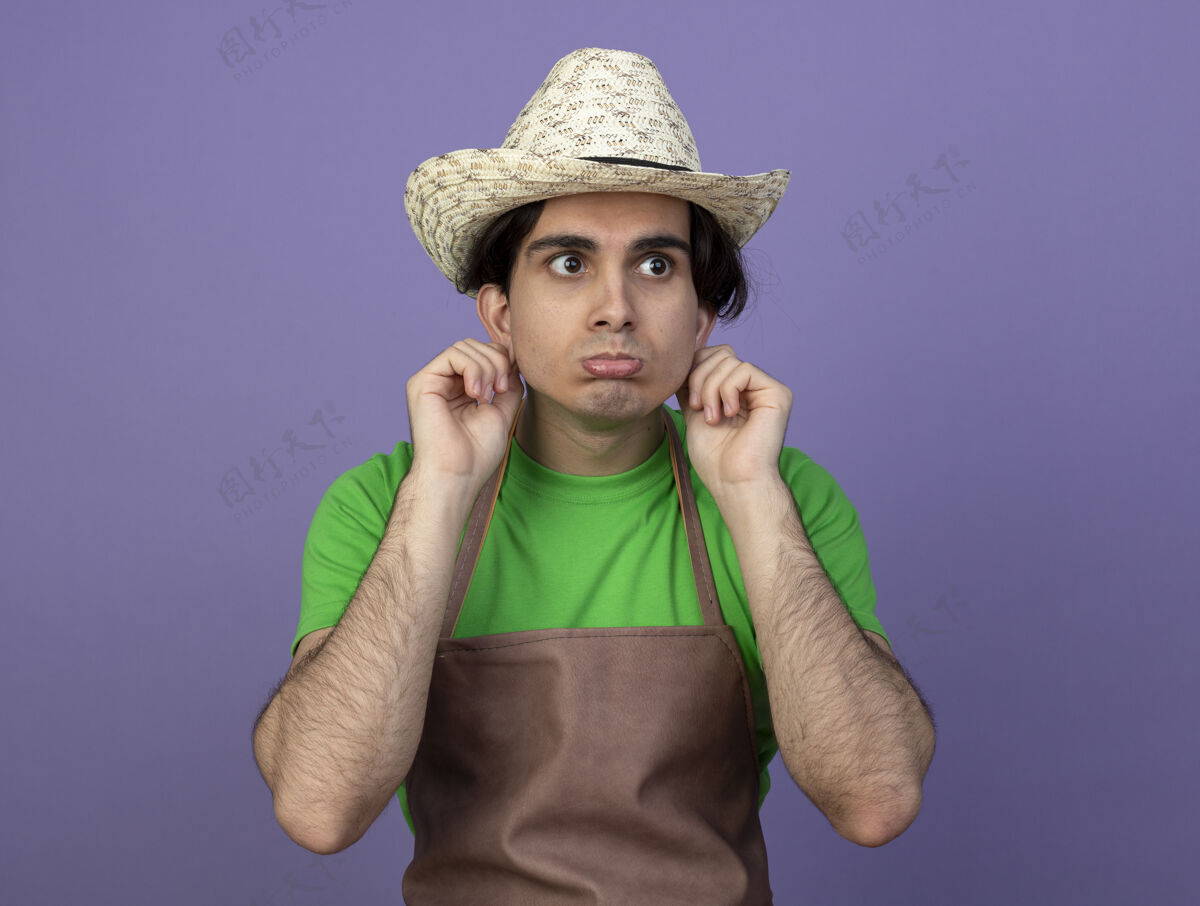 花园悲伤地看着身边穿着制服的年轻男园丁 戴着园艺帽 抱着紫色的耳朵孤立着年轻紫色帽子
