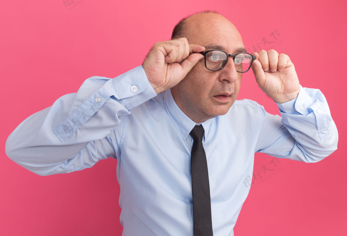 惊喜惊讶地看着旁边的中年男子 穿着白色t恤 打着领带 戴着眼镜 隔离在粉红色的墙上眼镜中年领带