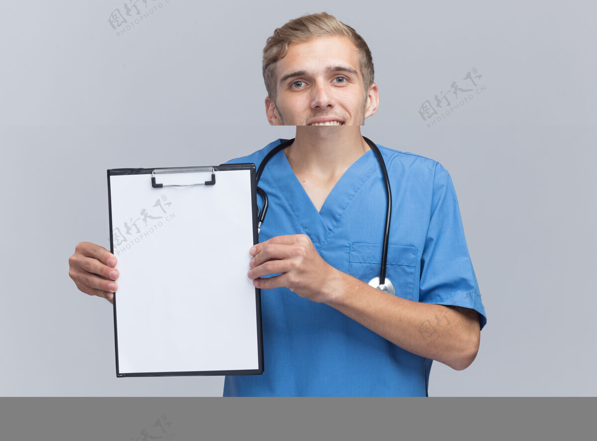 男性微笑着的年轻男医生穿着医生制服 听诊器拿着剪贴板隔离在白墙上听诊器剪贴板微笑