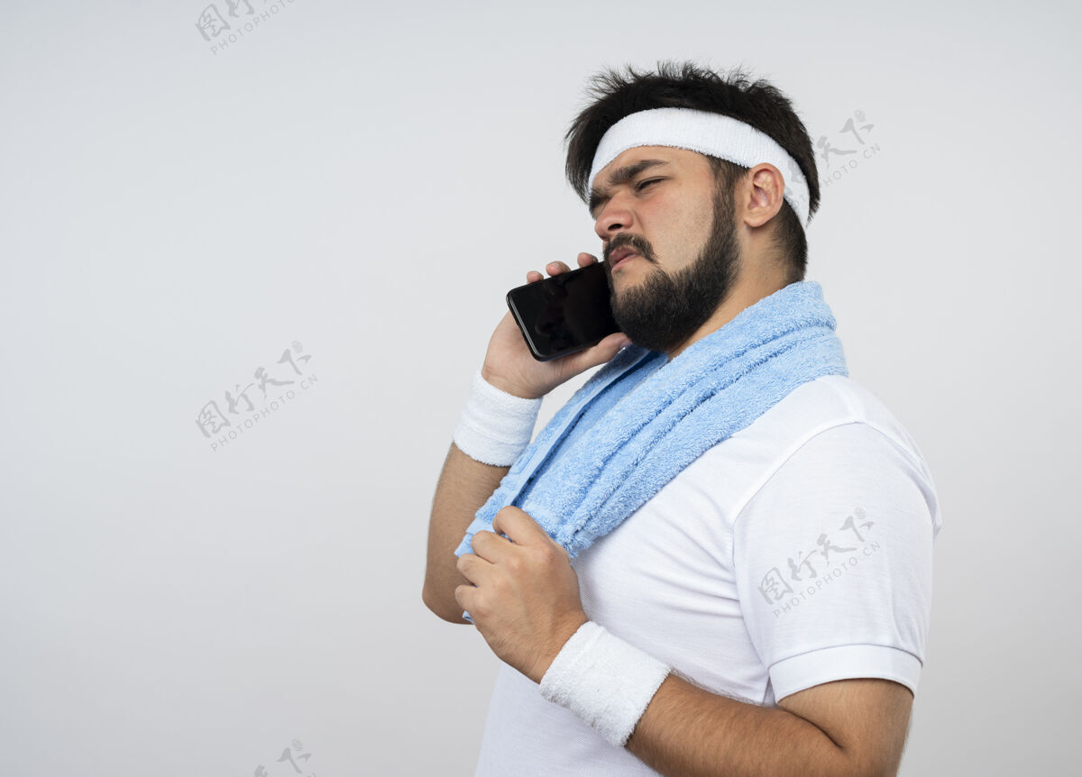 说话困惑的年轻人戴着头带和手镯 肩上带着毛巾 在白色的墙壁上讲着电话 并留有复印空间毛巾头带男人