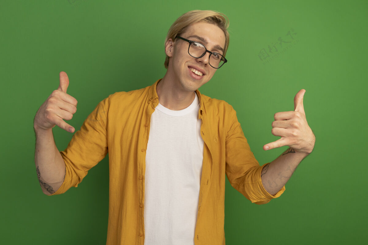 绿色微笑着的年轻金发小伙子穿着黄色t恤 戴着眼镜 在绿色屏幕上显示着打电话的手势手势黄色男人