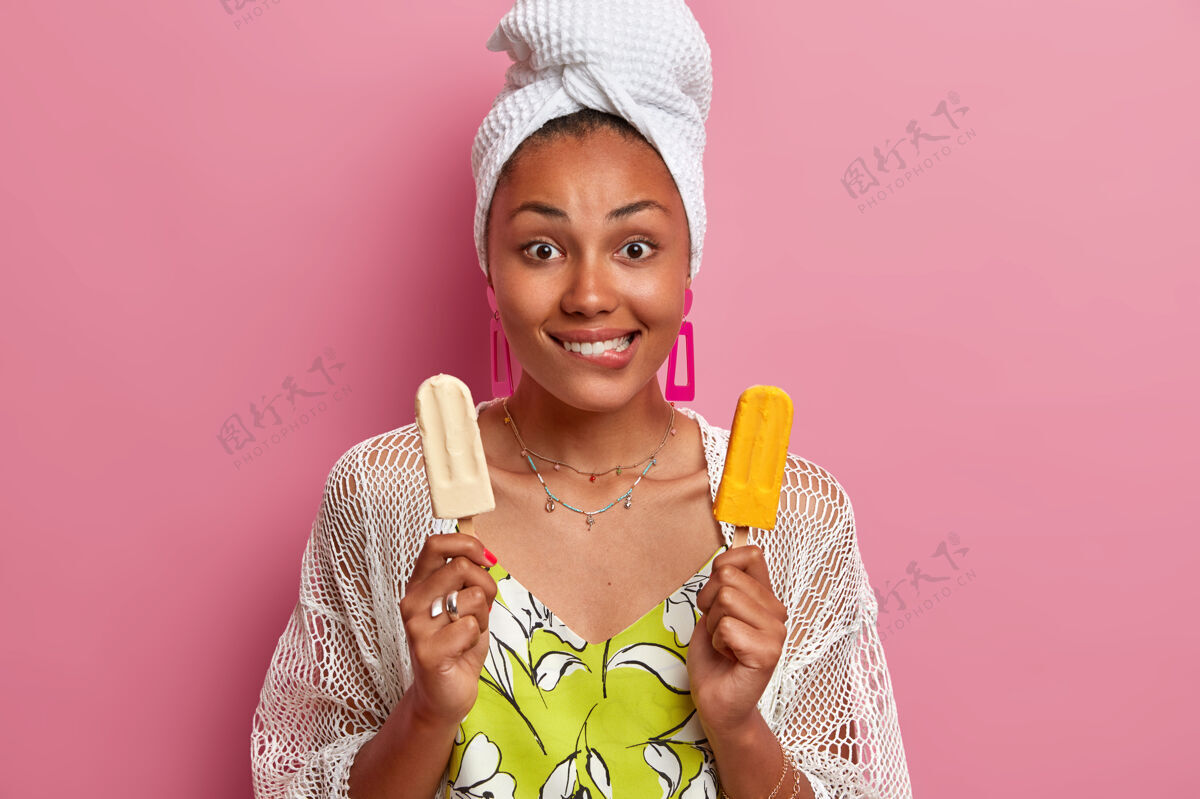 人年轻的非洲裔美国妇女咬嘴唇的肖像令人惊讶地看着相机拿着两个美味的冰淇淋棒美味水平高兴