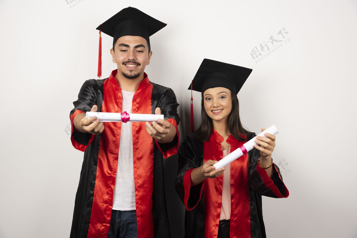 女穿着长袍的应届毕业生看着他们白色的毕业证书年轻成功长袍