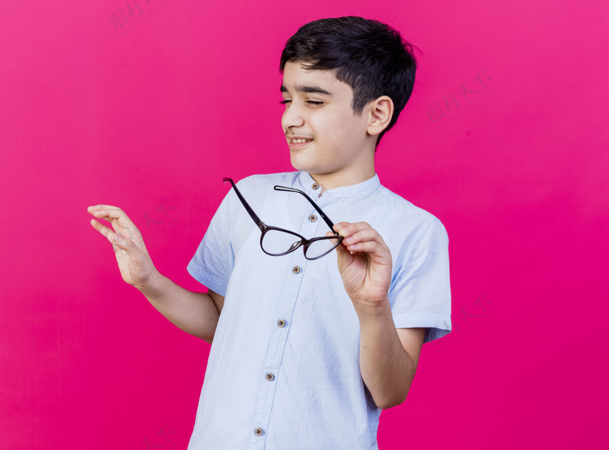 手未戴眼镜的小男孩 手举在空中 闭着眼睛 在粉红色的墙上做着不孤立的手势 还有复印空间眼镜人空气