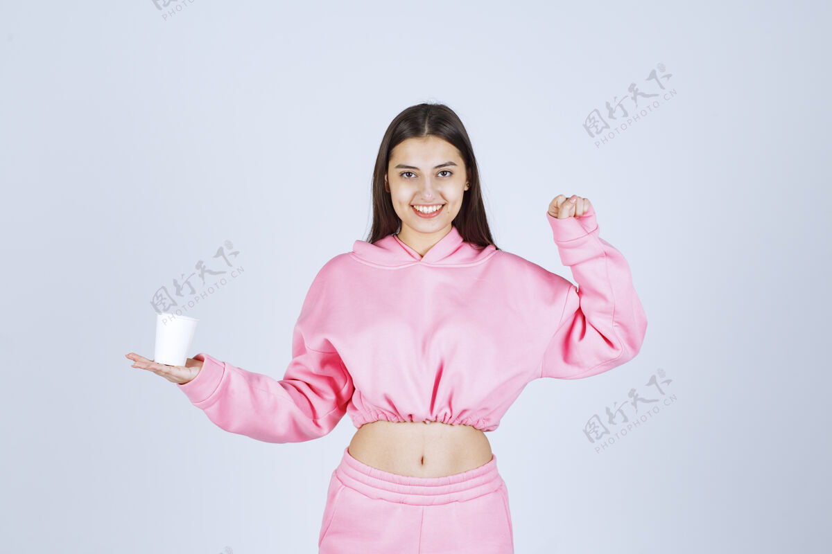 健康穿着粉色睡衣的女孩拿着咖啡杯 伸出拳头人成人力量