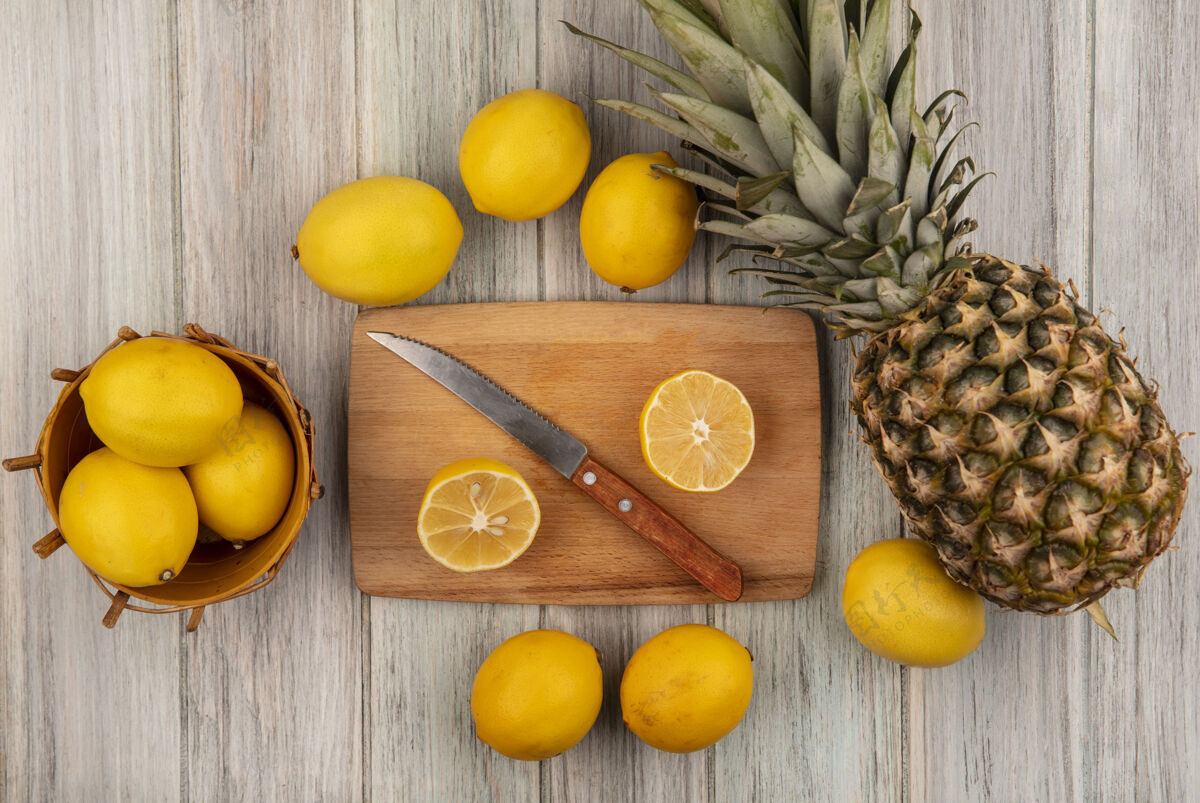 刀健康的柠檬放在桶上 半个柠檬放在木制的厨房板上 刀子上的柠檬和菠萝被隔离在灰色的木制背景上视图切片水果