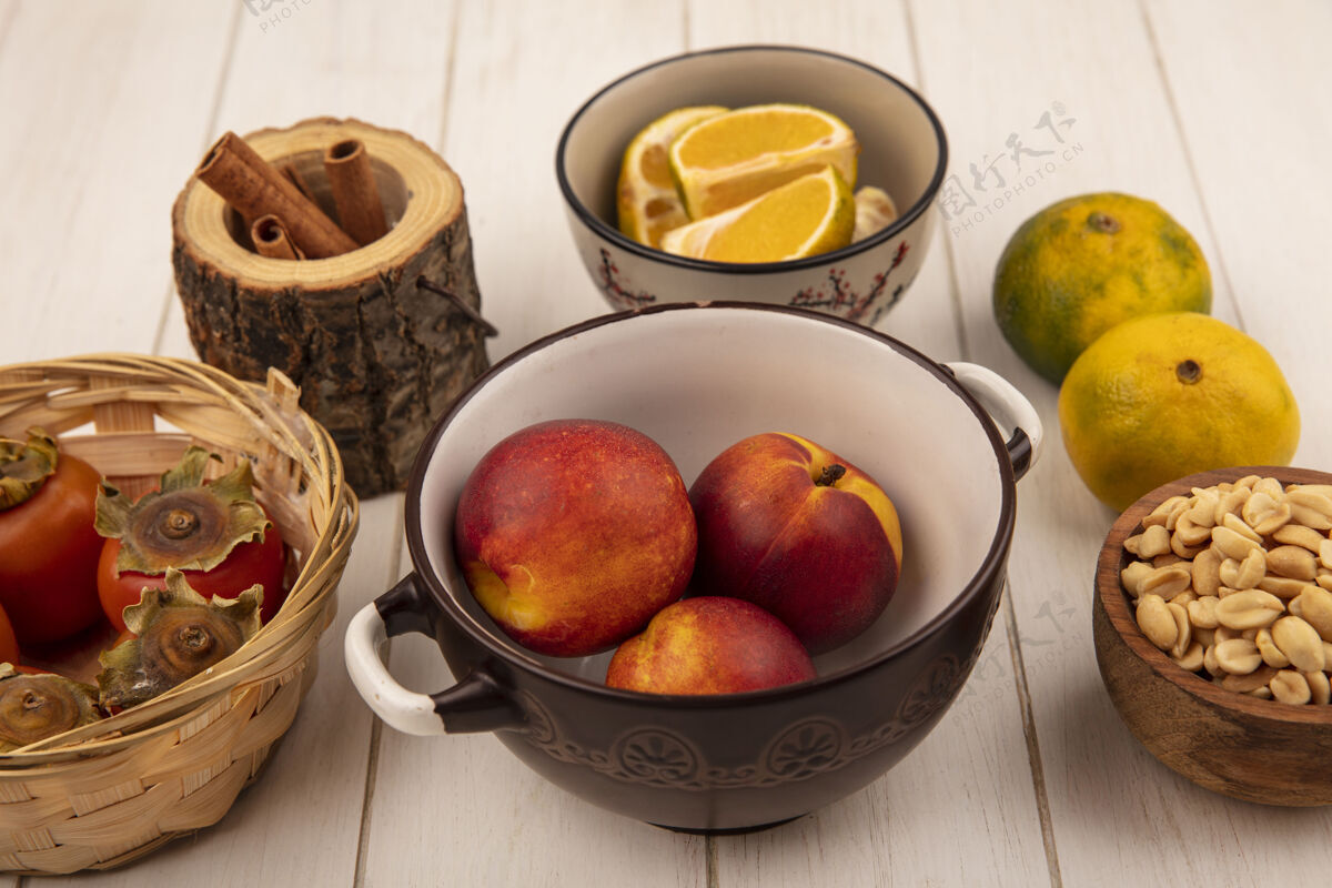 顶部顶视图新鲜的桃子放在一个碗里 柿子放在一个桶里 花生放在一个木碗里 背景是白色的木头桃柿子碗